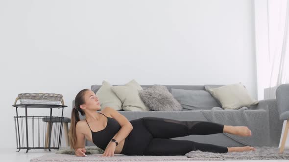 Young Woman Is Doing Exercises Rising Leg Up Lying on Side on Carpet at Home.