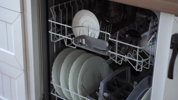 A Woman Opens a Dishwasher and Takes Out Clean Dishes