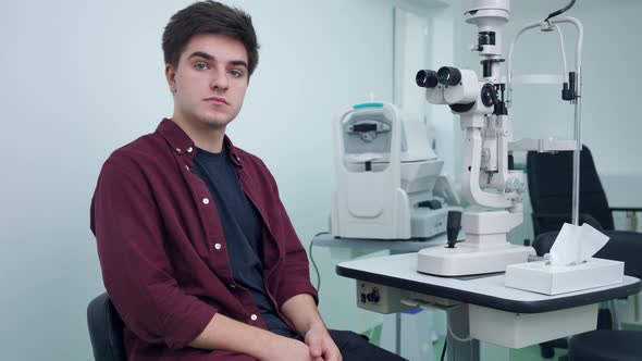 Medium Shot Portrait of Young Caucasian Man Sitting in Ophthalmologic Clinic at Retina Camera Posing alt