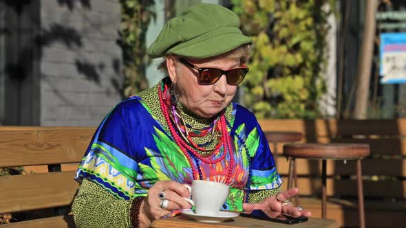 Senior woman drinks coffee and texts on the phone