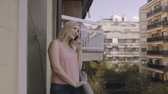 Young adult female tourist talking on smart phone on balcony in Barclona