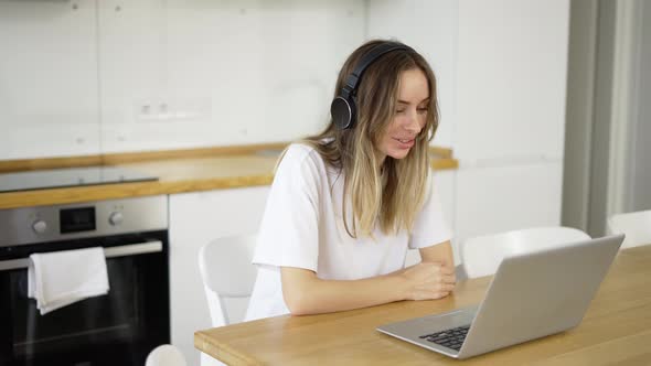 Blonde Woman Make Video Call Online Using Laptop and Headphones at Kitchen alt