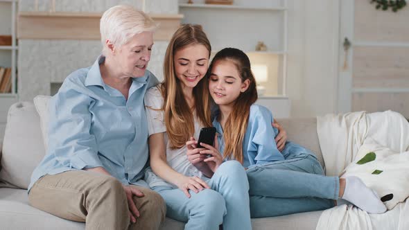 Adorable School Kid Girl Sitting on Sofa with Young Mother and Smiling Mature Older Granny Playing alt
