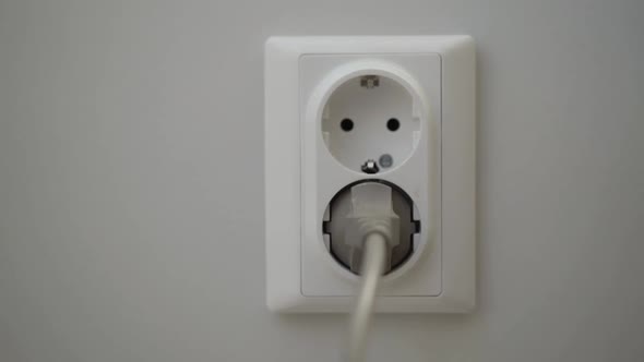 Female Hand Puts a Power Plugs in the Wall Socket alt