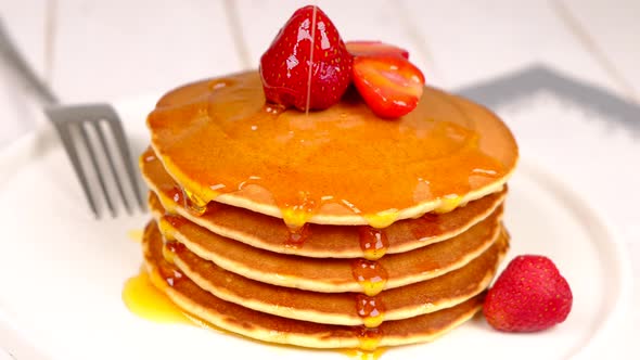 Pancakes Poured with Honey Decorated with Strawberries on a White Background