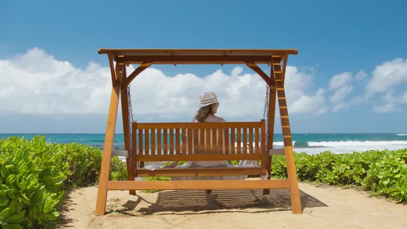 Back View Young Relaxed Woman Swaying Sitting on Swings with Ocean Beach View alt