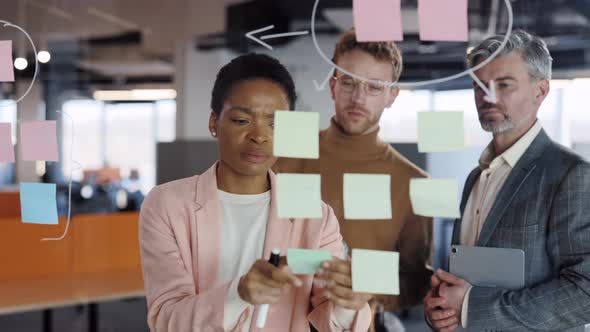 Close Up of Female Office Worker Using Glass Board and Proposing Her Problem Solving to Workmates alt