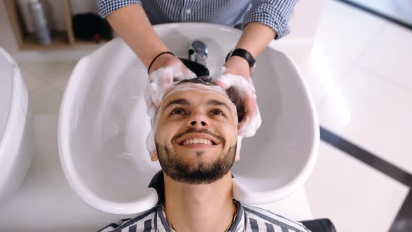 Happy Charismatic Young Man at the Barber Shop While the Man Washes His Hair alt