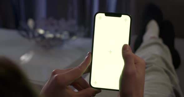 Woman Rests on the Sofa and Uses Smartphone Scrolls Through the Images and Swipe Across the Green alt
