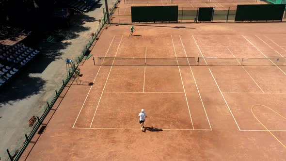 Tennis clay court seen from above with two men playing match. They are mature adult alt
