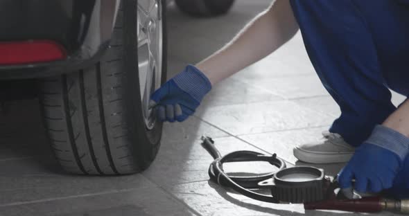 Female mechanic doing a car service in the auto repair shop, she is checking tire pressure