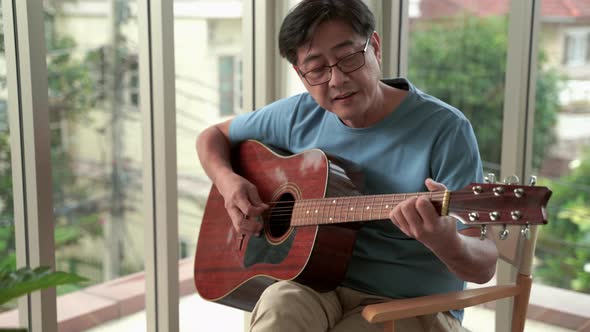 elderly Asian man resting playing guitar in the living room.