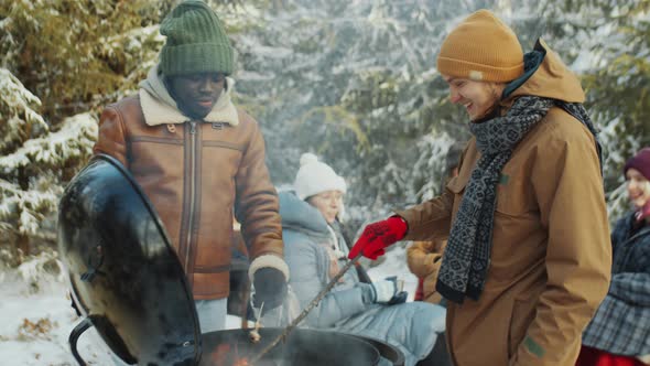 Men Eating and Chatting by BBQ Grill on Winter Picnic in Woods alt