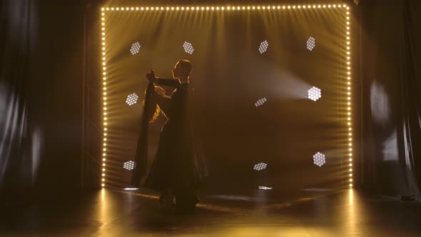 Young Couple Elegantly Dancing Waltz and Moving Smoothly in Studio with Neon Spotlights. Silhouettes alt