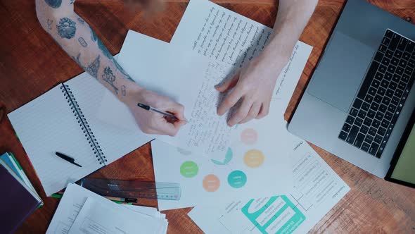 Young Man Searching Through Textbooks and Notes Writing on the Laptop alt