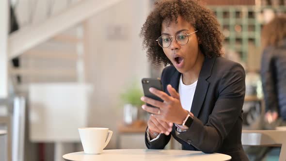 Upset African Businesswoman Reacting to Loss on Smartphone at Cafe alt