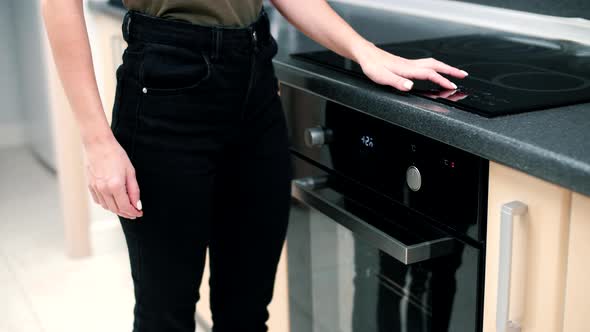 Skinny girl in a modern bright kitchen turns on the touch stove