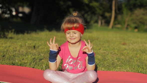 Child Sitting on Mat and Performing Yoga Meditation Outdoors in Park. Girl Doing Yoga Exercises alt