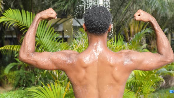 Back Portrait of a Black Man Showering Outdoor in Tropical Plants Background alt