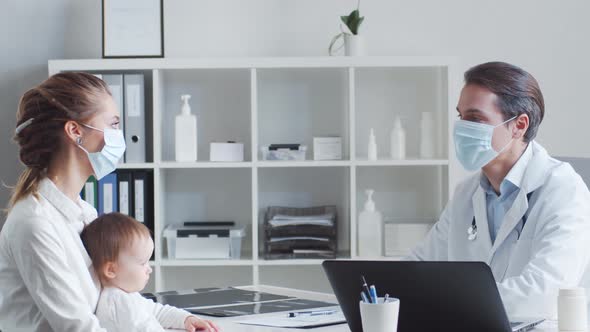 Male pediatrician is examining little baby. Doctor, mother and daughter in medical office. alt