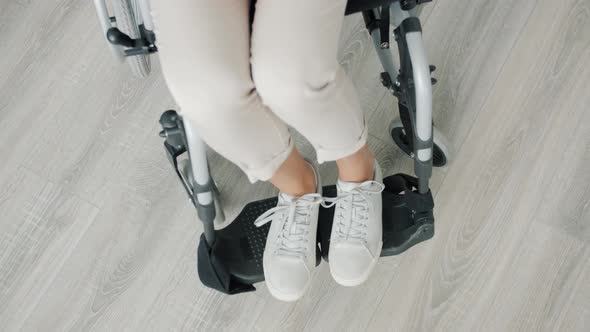 High Angle View of Female Feet of Paraplegic Woman Sitting in Wheelchair Indoors alt