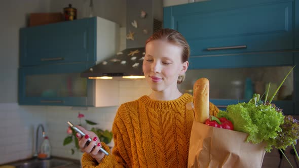 Young Woman with Groceries Bag in Hands Kitchen Shows Phone Green Screen alt