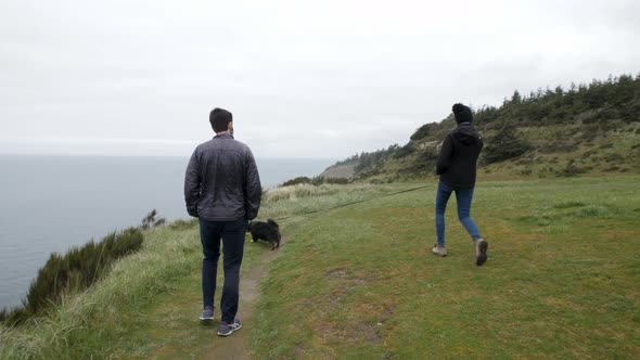 Couple walks along a bluff overlooking the Pacific Ocean with the dog. alt