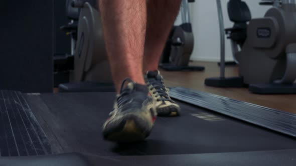 A Fit Man Walks on a Treadmill in a Gym - Front Closeup on the Feet alt