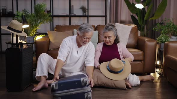 Elderly couple in Asia packs clothes in their luggage at home to prepare for their vacation.