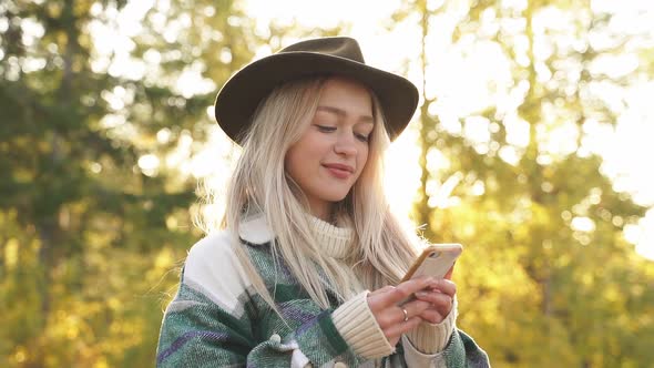 Portrait of Cute Tourist Girl in Autumn Forest with Smartphone in Her Hands