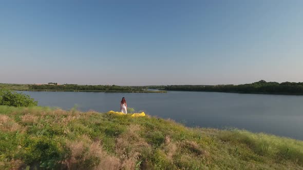 A Girl with Loose Hair in a Dress Stands on the High Bank of the Lake
