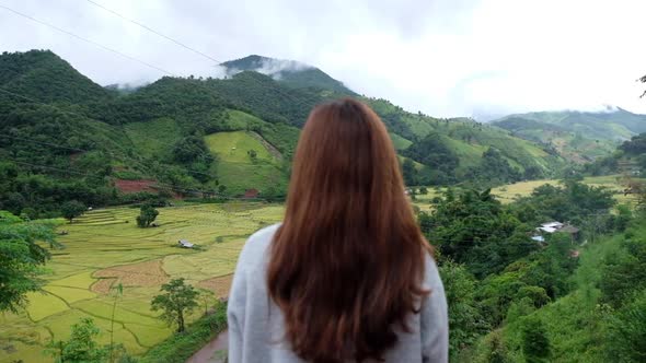 Slow motion rear view of a woman looking at a paddy field or rice terrace with mountain views