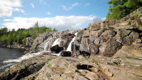 Cascading waterfall flows down rock face into lake basin on bright sunny day in Muskoka Ontario alt
