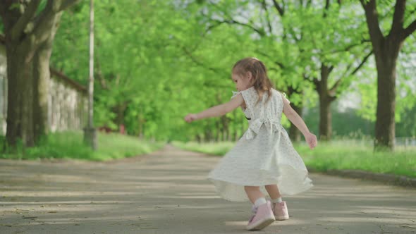 Cheerful Caucasian Girl Spinning and Jumping in Sunny Summer Park. Wide Shot Portrait of Pretty alt