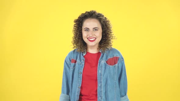 Curly Girl Smiles Broadly and Winks on Yellow Background at Studio, Slow Motion alt