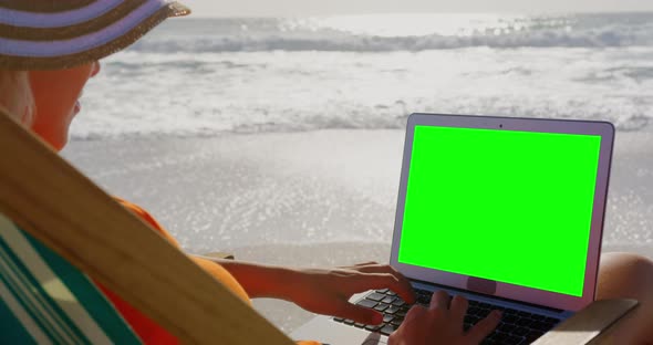 Woman with hat using laptop at beach in the sunshine 4k