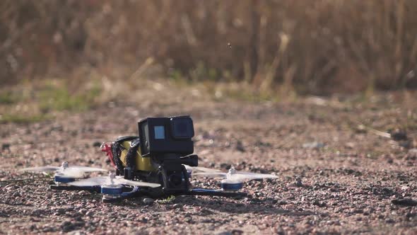 FPV Racing Drone Takes Off From a Dirt Surface Raising Dust and Stones