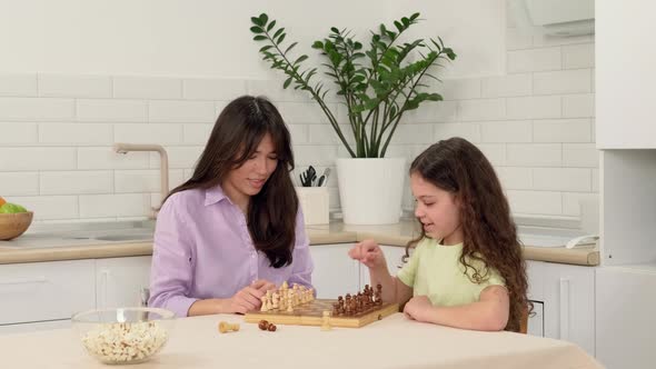 Young Mother Teaches Her Daughter to Play Chess Sitting at the Table at Home alt