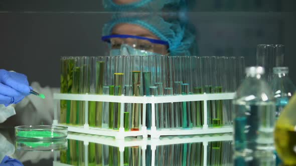 Researcher Adding Green Powder in Tube With Yellow Liquid and Checking Reaction alt