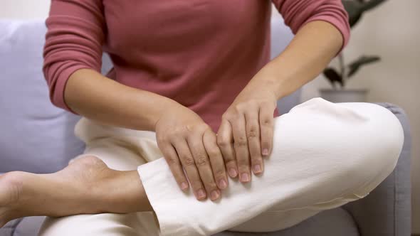 Woman sitting on the sofa at home performing self massage. alt