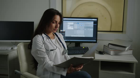 Female Doctor is Sitting at a Table and Studying a Patient's Medical History alt