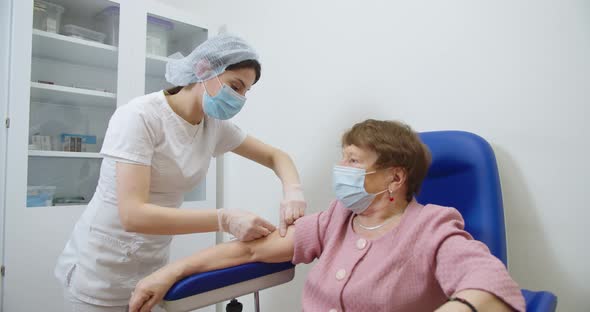 Nurse Wearing Protective Gloves and a Protective Mask Gives a Vaccine Injection to a Old Female