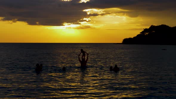 Black silhouette of family playing in the sea. alt