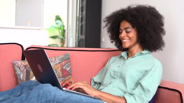 African Young Woman Student or Freelancer in Casual Wear Sitting on the Couch and Using Laptop