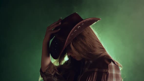 Girl in a Cowboy's Clothes Is Dressing a Hat. Black Smoke Background. Slow Motion alt