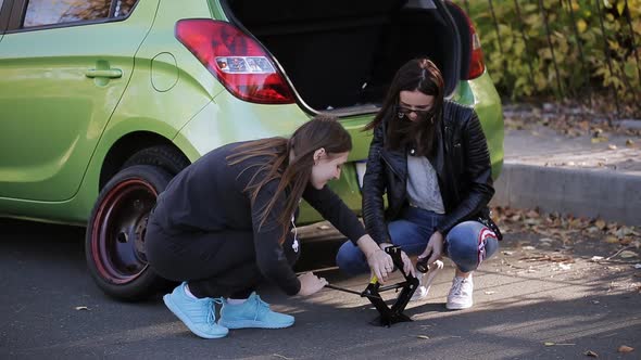 Two Women Know How to Operate the Jack to Change a Punctured Wheel of the Car