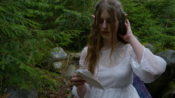An Elf Girl in a White Dress Holds a Letter in Her Hands in the Forest alt