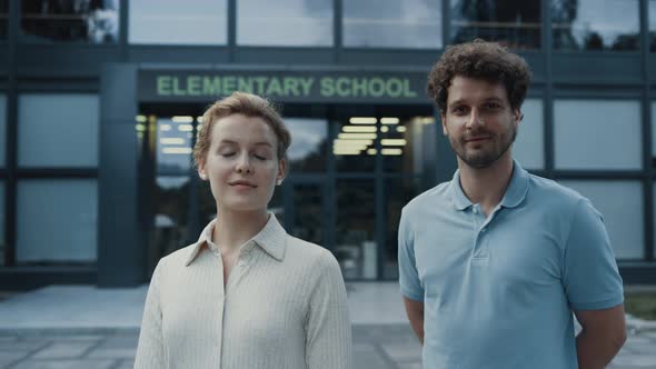 Couple Smiling Teachers Posing at Elementary School Entrance alt