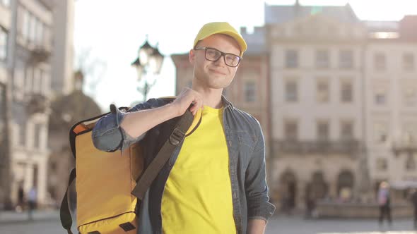 Portrait of a Happy Young Delivery Man Who is Standing and He Throws His Backpack Over His Shoulder alt