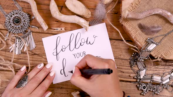 Woman's hand writing FOLLOW YOUR DREAM with bohemian decorations around alt